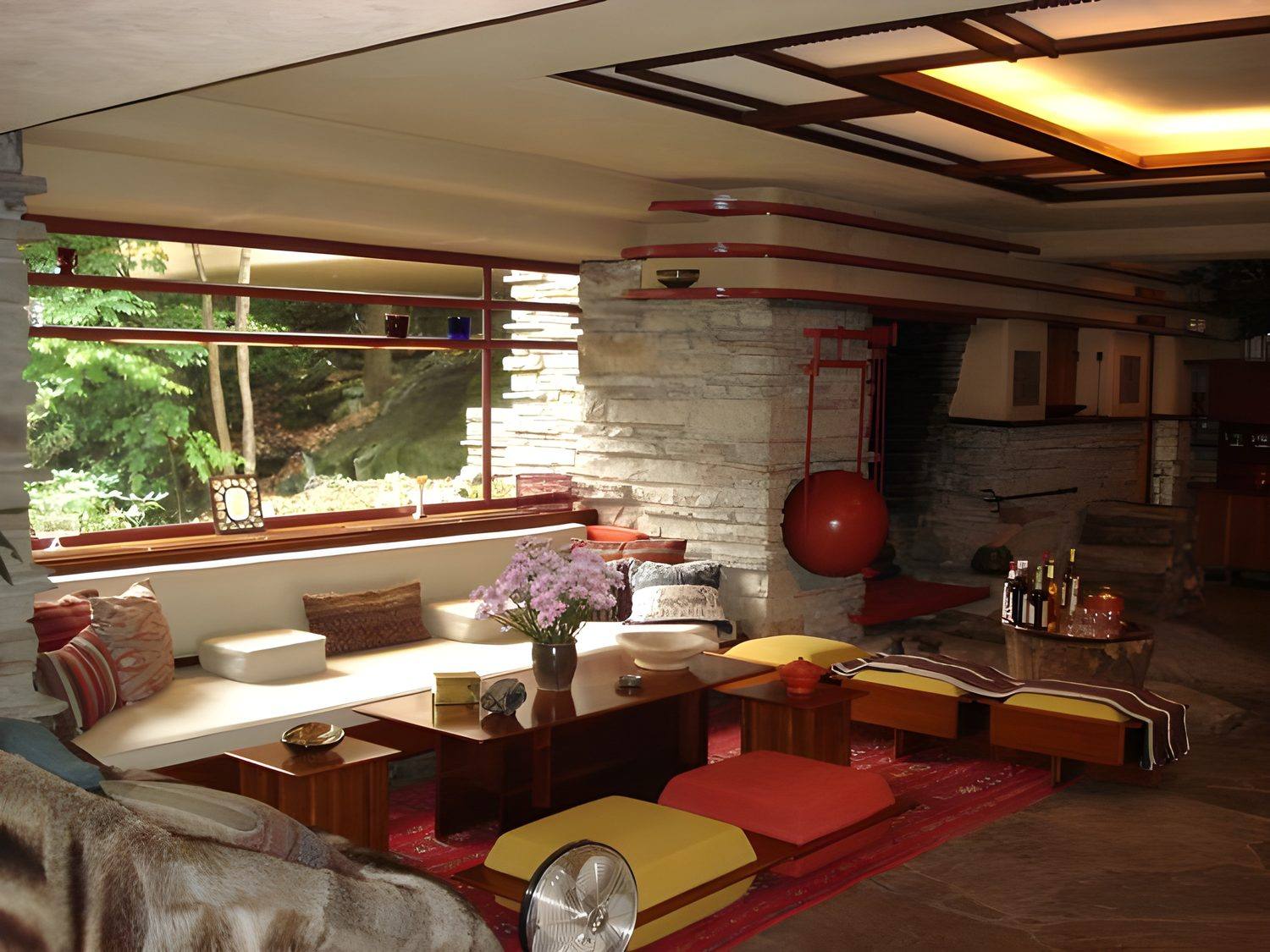 The living room at Fallingwater, with the natural boulder of the site rising through the floor to form the hearth before the stone fireplace.