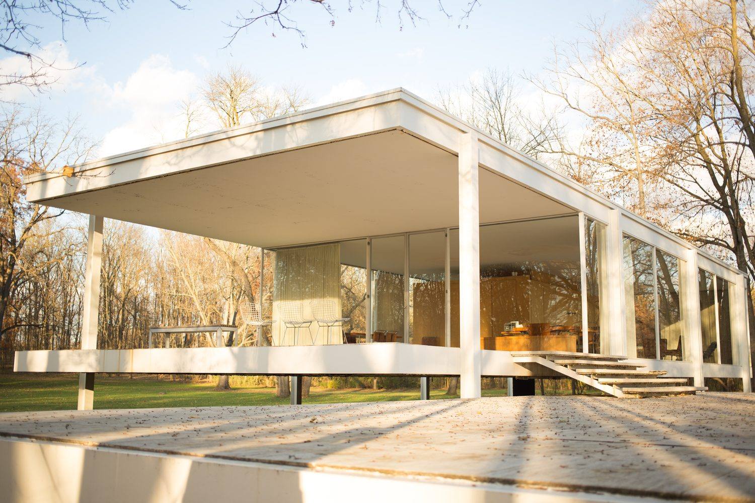 The travertine terrace and steps of the Farnsworth House rising to the glass pavilion, with bare trees behind.