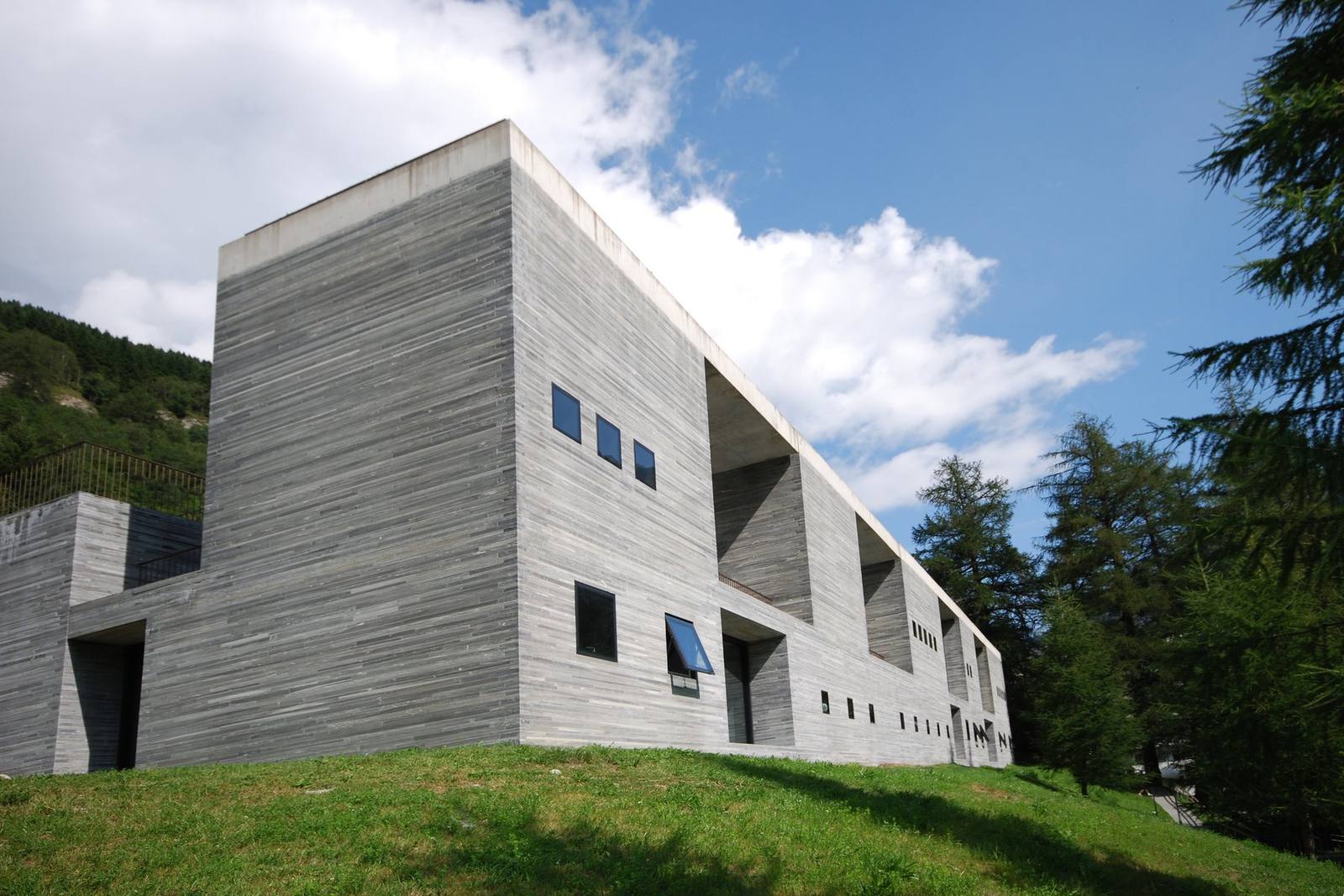 The layered Valser quartzite facade of Therme Vals, Switzerland, rising from the hillside meadow