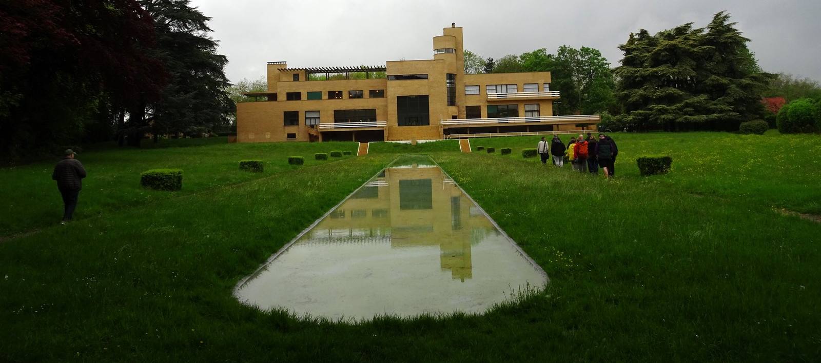South facade of Villa Cavrois in Croix, France, a long yellow brick modernist villa with a cylindrical belvedere tower, seen across the lawn with its reflecting pool.
