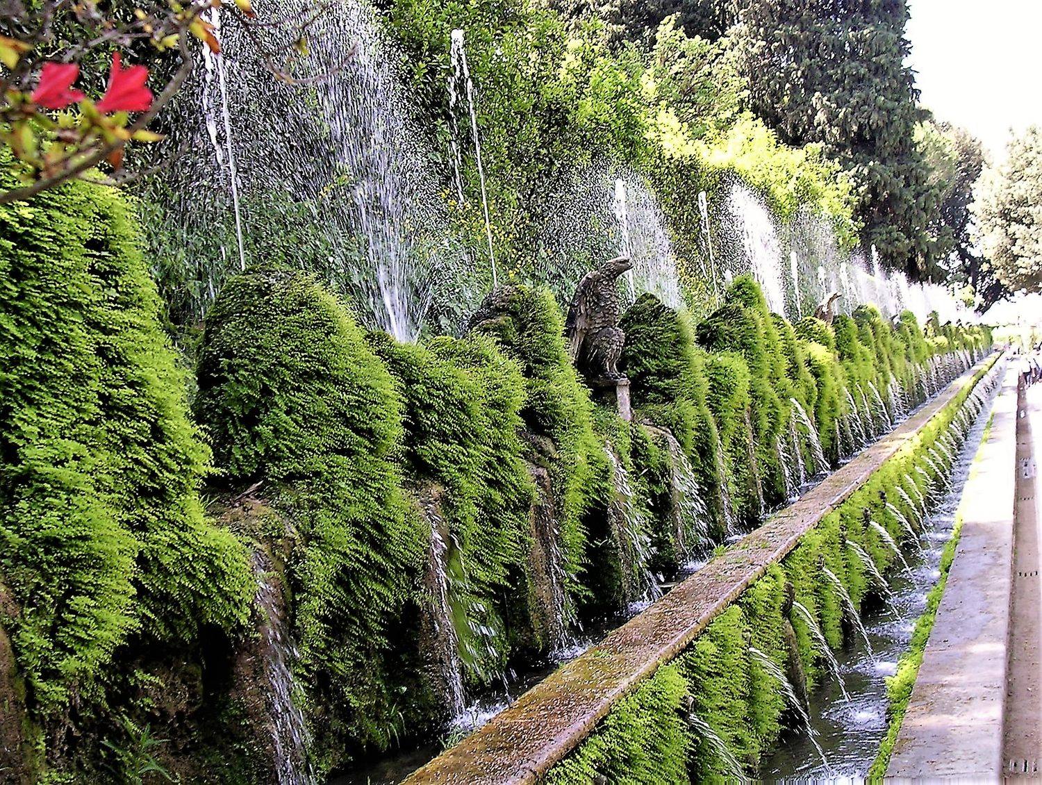 The Alley of the Hundred Fountains at Villa d'Este, water jets arching from a moss-covered wall into a long canal.